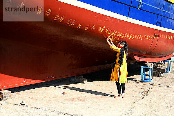 Die Tochter des Bootseigentümers vollzieht eine Puja auf dem neuen Boot  indem sie vor dem ersten Stapellauf Handabdrücke auf den Rumpf macht  Vanakbara  Gujarat  Indien  Asien