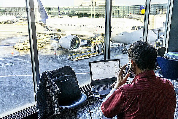 Rückansicht eines reifen Mannes  der Laptop und Smartphone benutzt  während er auf dem Flughafen wartet  Norwegen  Skandinavien  Europa