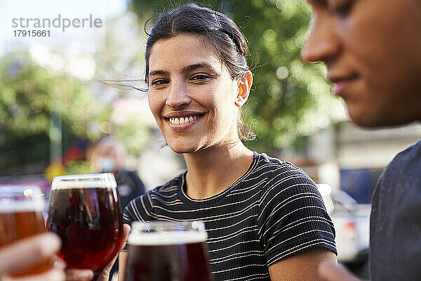 Porträt einer glücklichen jungen lateinamerikanischen Frau  die in die Kamera lächelt und ein Glas Bier hält