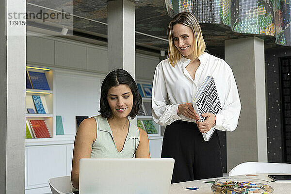 Mittelaufnahme einer lateinamerikanischen Innenarchitektin und ihrer Assistentin  die auf einen Laptop-Bildschirm schauen