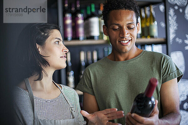 Mitarbeiterin eines Spirituosengeschäfts diskutiert mit einem Kunden über eine Weinflasche