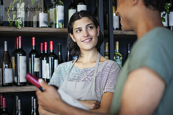 Weibliche Angestellte in einer Weinhandlung mit Schürze hört einer Mitarbeiterin zu