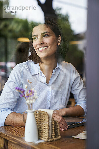 Porträtaufnahme durch das Fenster einer lächelnden lateinamerikanischen Frau  die in einem Café sitzt