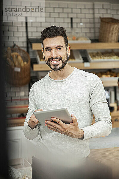 Bäckereibesitzer hält ein digitales Tablet in der Hand und blickt in die Kamera