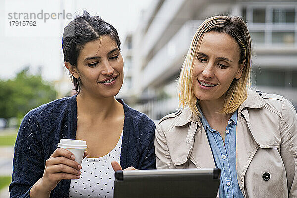 Mittelaufnahme von zwei Unternehmerinnen  die ihre Arbeit auf einem digitalen Tablet im Freien überprüfen