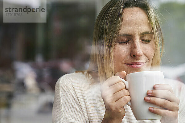 Porträt einer Frau mit geschlossenen Augen  die eine Tasse Kaffee genießt