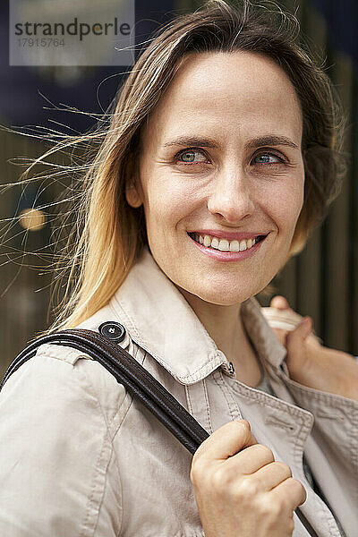 Mittelaufnahme einer lächelnden Frau mit Handtasche  die in die Ferne schaut
