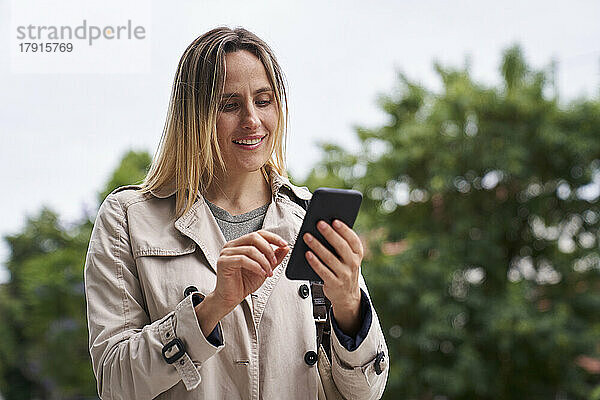 Attraktive Frau schaut auf ihr Handy  während sie auf der Straße geht
