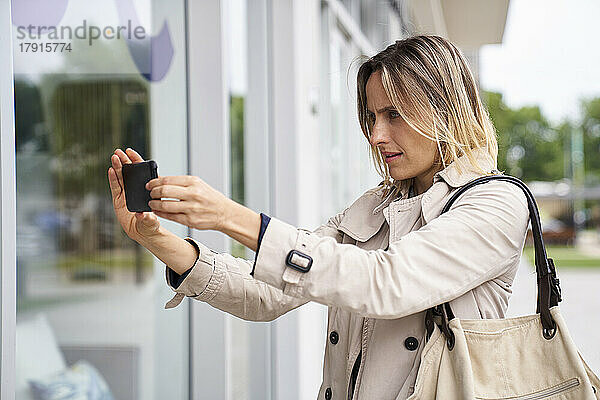 Mittlere Einstellung einer Frau  die ein Schaufenster mit ihrem Mobiltelefon fotografiert