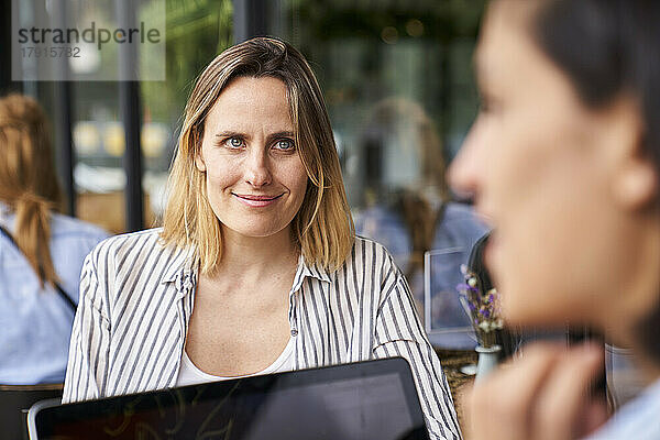 Vorderansicht einer Unternehmerin bei der Arbeit mit ihrem lateinamerikanischen Partner  von hinten gesehen unscharf