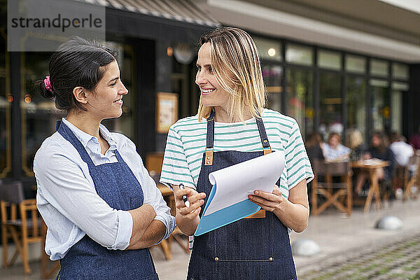 Mid-shot von zwei Restaurantbesitzerinnen  die vor ihrem Restaurant eine Liste prüfen