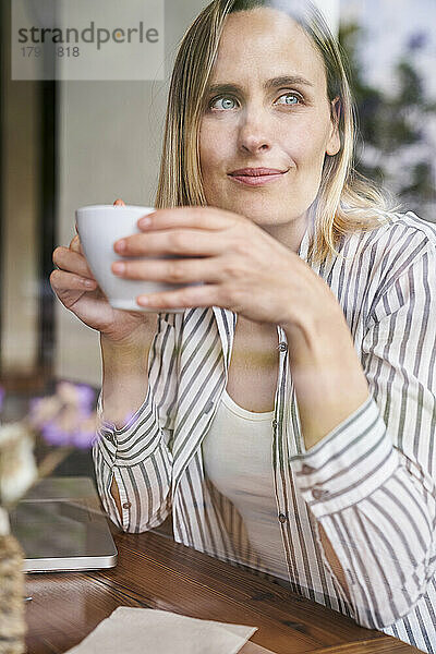 Mittelaufnahme einer attraktiven Frau  die in einem Café eine Tasse Kaffee genießt