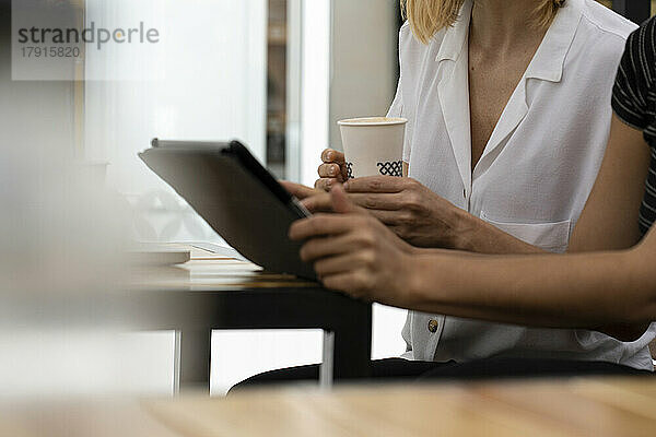 Mittelaufnahme der Hände einer Unternehmerin bei der Arbeit an einem Laptop und einem digitalen Tablet