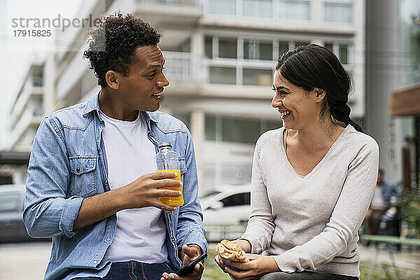 Junger afroamerikanischer Mann und lateinamerikanische Frau  die im Freien einen Snack zu sich nehmen und sich amüsieren