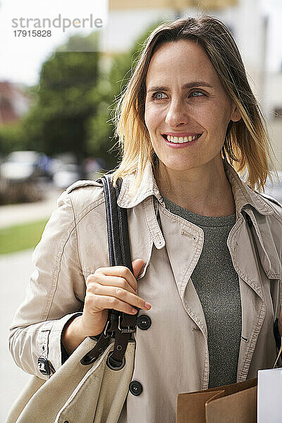 Mid-shot von lächelnden Frau hält ihre Handtasche beim Gehen auf der Straße