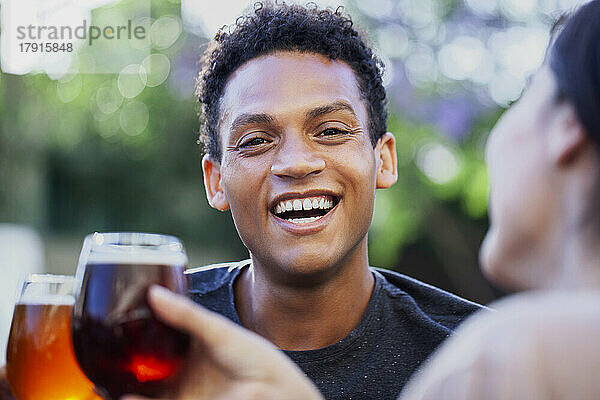 Lateinamerikanischer junger Mann schaut in die Kamera  während er mit Freunden Bier trinkt