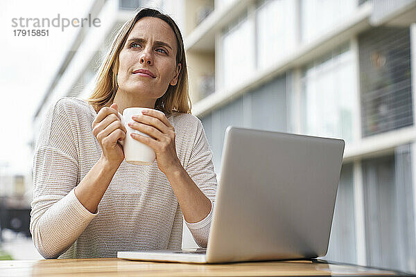 Niedriger Blickwinkel auf eine Unternehmerin  die mit einem Laptop arbeitet und Kaffee trinkt