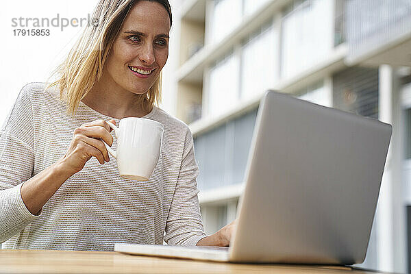 Niedriger Blickwinkel auf eine Unternehmerin  die auf einen Laptop-Bildschirm schaut und Kaffee trinkt