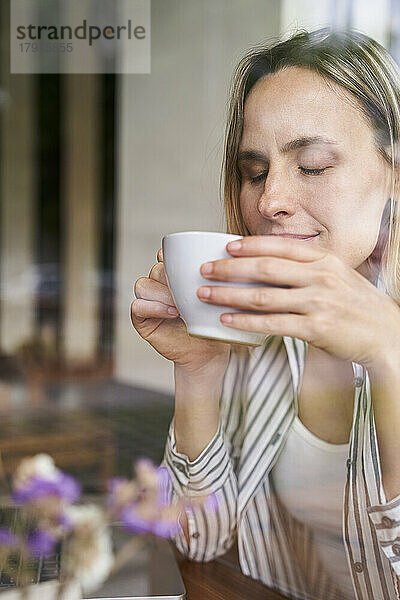 Porträt einer attraktiven Frau  die mit geschlossenen Augen eine Tasse Kaffee in den Händen hält