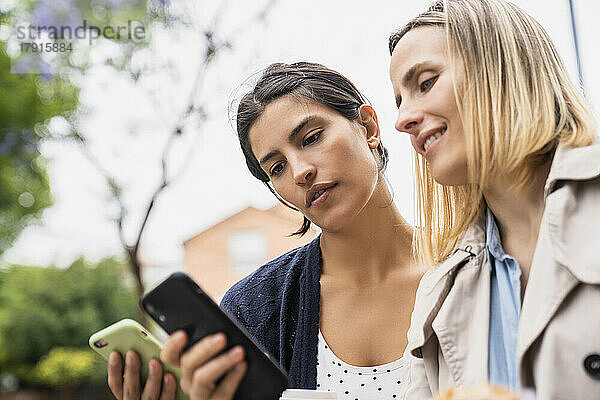 Niedrige Seitenansicht von zwei Unternehmerinnen  die bei der Arbeit im Freien Informationen über ihre Smartphones austauschen