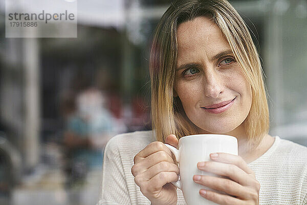 Porträt einer attraktiven Frau  die eine Tasse Kaffee in der Hand hält und den Moment genießt  in der Mitte der Aufnahme