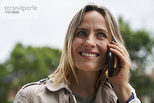 Nahaufnahme einer lächelnden Frau  die auf der Straße mit einem Handy telefoniert