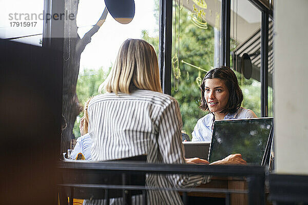 Mid-shot von zwei Unternehmerinnen  die sich in einem Café über ihr Geschäft unterhalten