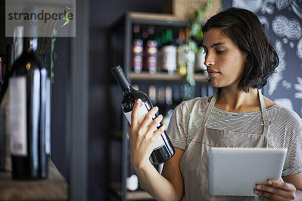 Mitarbeiterin eines Weinladens liest das Etikett einer Weinflasche