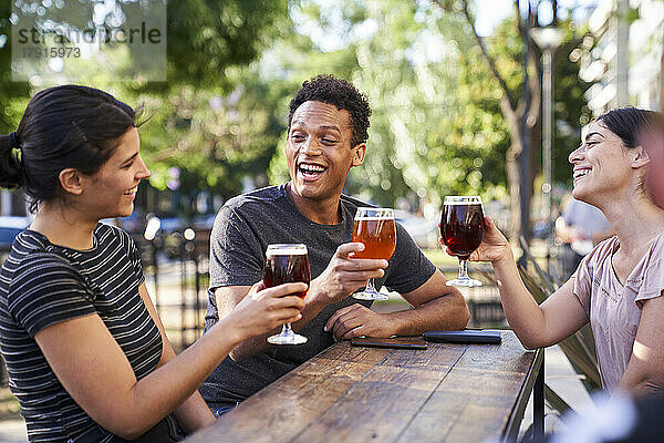 Mittlere Aufnahme von drei jungen  unterschiedlichen Freunden  die bei der Happy Hour mit ihren Bieren anstoßen