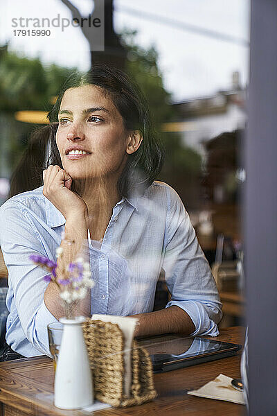 Durch ein Fenster aufgenommenes Foto einer in Gedanken versunkenen lateinamerikanischen Frau in einem Café