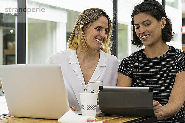 Mittlere Einstellung von zwei Unternehmerinnen  die mit einem Laptop und einem digitalen Tablet arbeiten