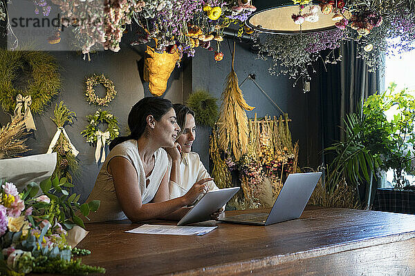 Weitblick auf zwei verschiedene Inhaberinnen eines Einrichtungsgeschäfts bei der Arbeit mit Laptop und digitalem Tablet