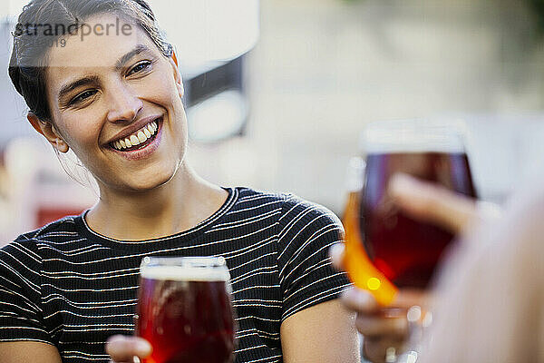 Lächelnde junge erwachsene Frau  die mit Freunden auf Bierbecher anstößt