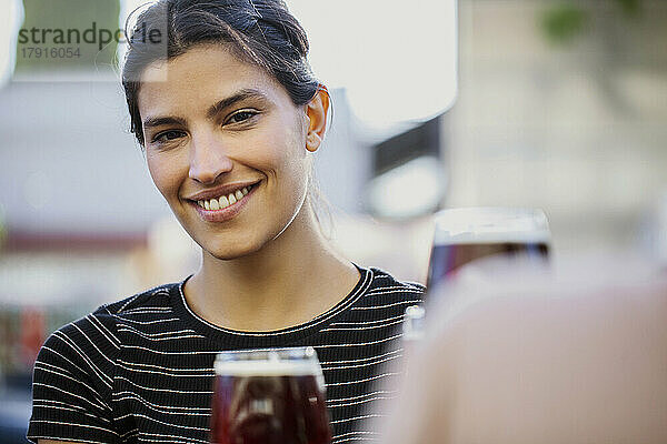 Junge Frau lächelt und schaut in die Kamera  während sie an einer Bar im Freien sitzt