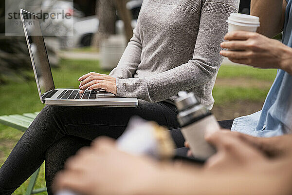 Mittelaufnahme einer Gruppe von Menschen und einer Frau  die einen Laptop auf ihrem Schoß hält und darauf tippt