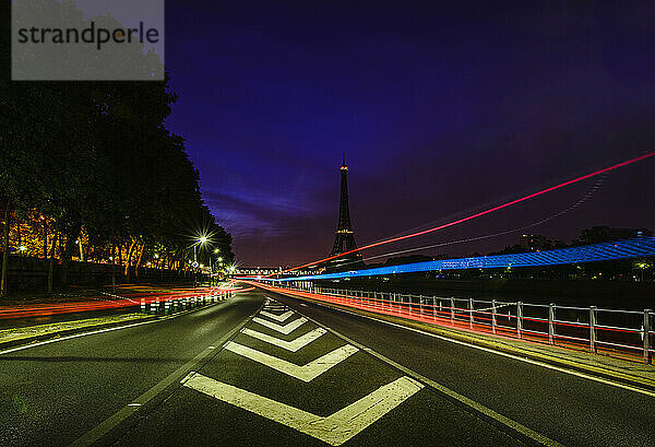 Straßenmarkierungen und farbige Lichtspuren bei Nacht auf einer geraden Straße in Paris.