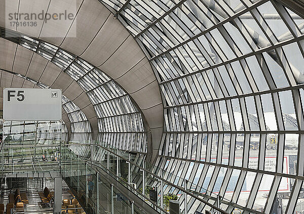 Abflug-Gate am Flughafen Bangkok  ein Blick von oben auf eine gebogene Glaswand des Terminals und den Wartebereich.