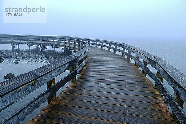 Eine Uferpromenade über das Wasser  Nebel steigt vom Meer auf.