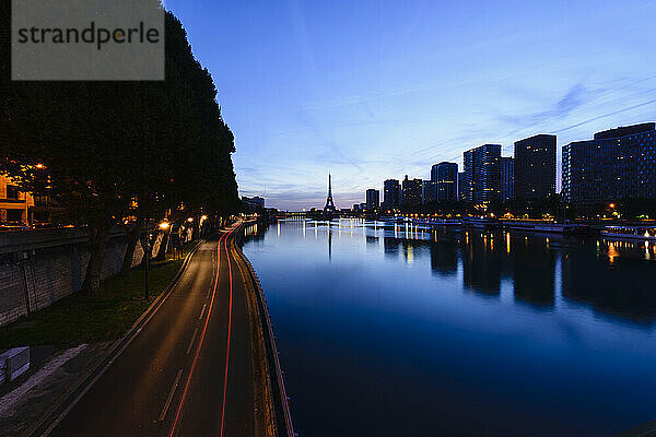 Blick entlang der Seine auf den Eiffelturm  die Uferpromenade und die Stadt in der Abenddämmerung  Spiegelungen auf dem Wasser.