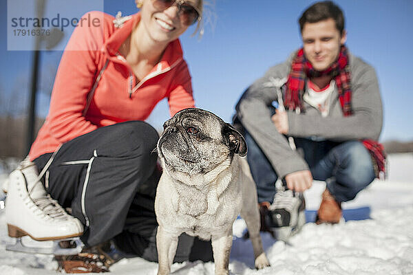 Pärchen kniend im Schnee mit Mops.