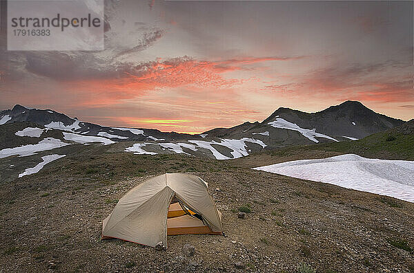Ein kleines Zelt  das bei Sonnenuntergang in der Wildnis von Mount Baker an einem Abhang knapp unterhalb der Schneegrenze aufgestellt wurde.