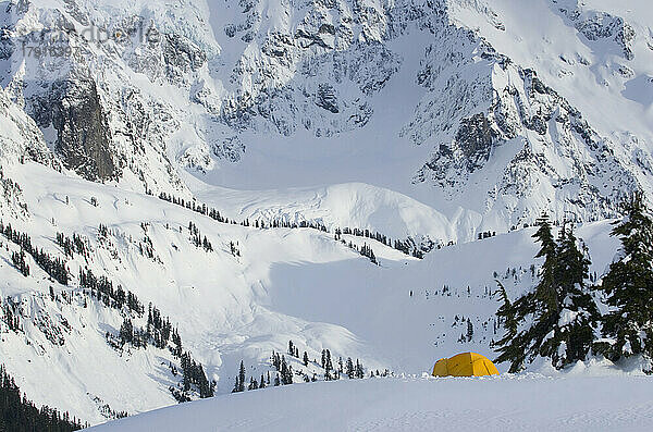 Ein kleines gelbes Zelt  das im tiefen Schnee an einem Hang aufgestellt ist  mit Blick auf die steilen Berghänge.