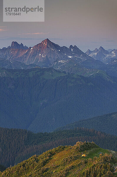 Blick von oben  ein kleines orangefarbenes Zelt auf einem Bergrücken  mit Blick ins Tal und auf die dahinter liegende Bergkette.