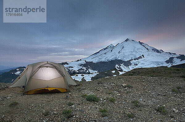Ein kleines Zelt  das bei Sonnenuntergang in der Wildnis von Mount Baker an einem Abhang knapp unterhalb der Schneegrenze aufgestellt wurde.
