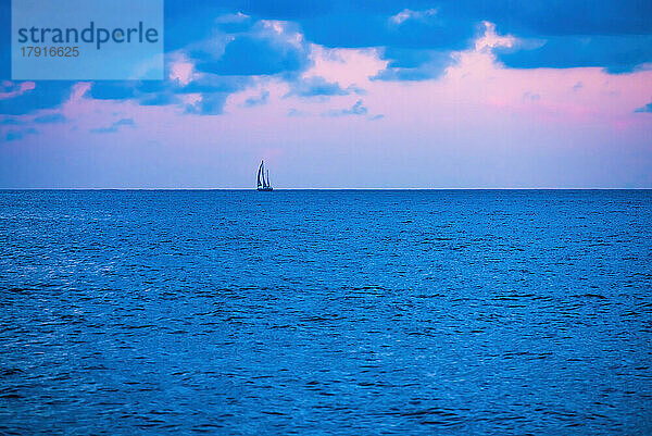 Ozean bei Sonnenaufgang mit einsamem Segelboot in der Ferne