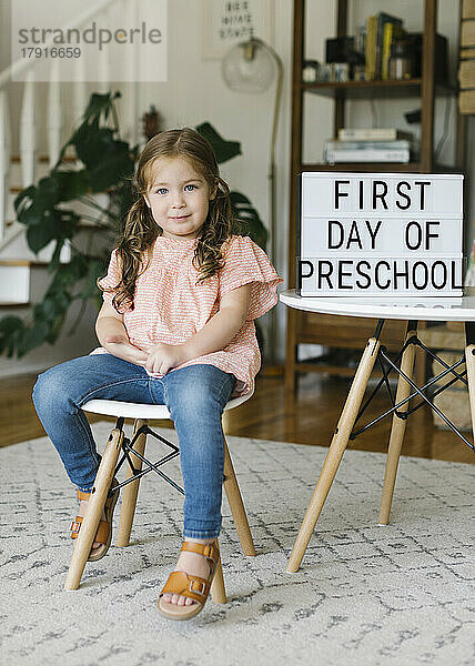 Porträt eines Mädchens (2-3)  das am Schild „Erster Tag der Vorschule“ sitzt