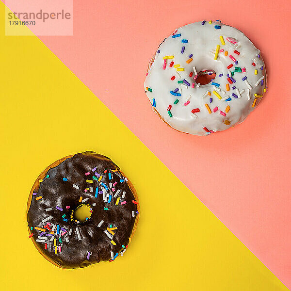 Draufsicht auf zwei Donuts mit Zuckerguss und Streuseln auf mehrfarbigem Hintergrund