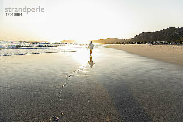 Südafrika  Hermanus  Teenager-Mädchen (16-17) spaziert bei Sonnenuntergang am Grotto Beach