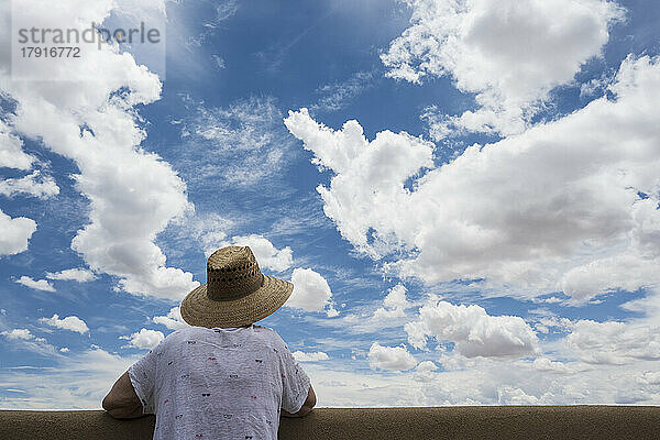 Rückansicht einer Frau  die über eine Mauer in den Wolkenhimmel blickt
