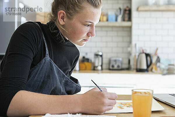 Teenager-Mädchen (16-17) arbeitet in der Küche an einem Aquarellbild